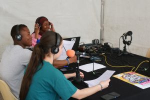 Photo du plateau radio avec casques et micros, et trois personnes autour de la table. 
