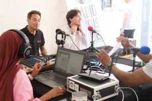 Photo du plateau radio avec casques et micros, et quatre personnes autour de la table. 